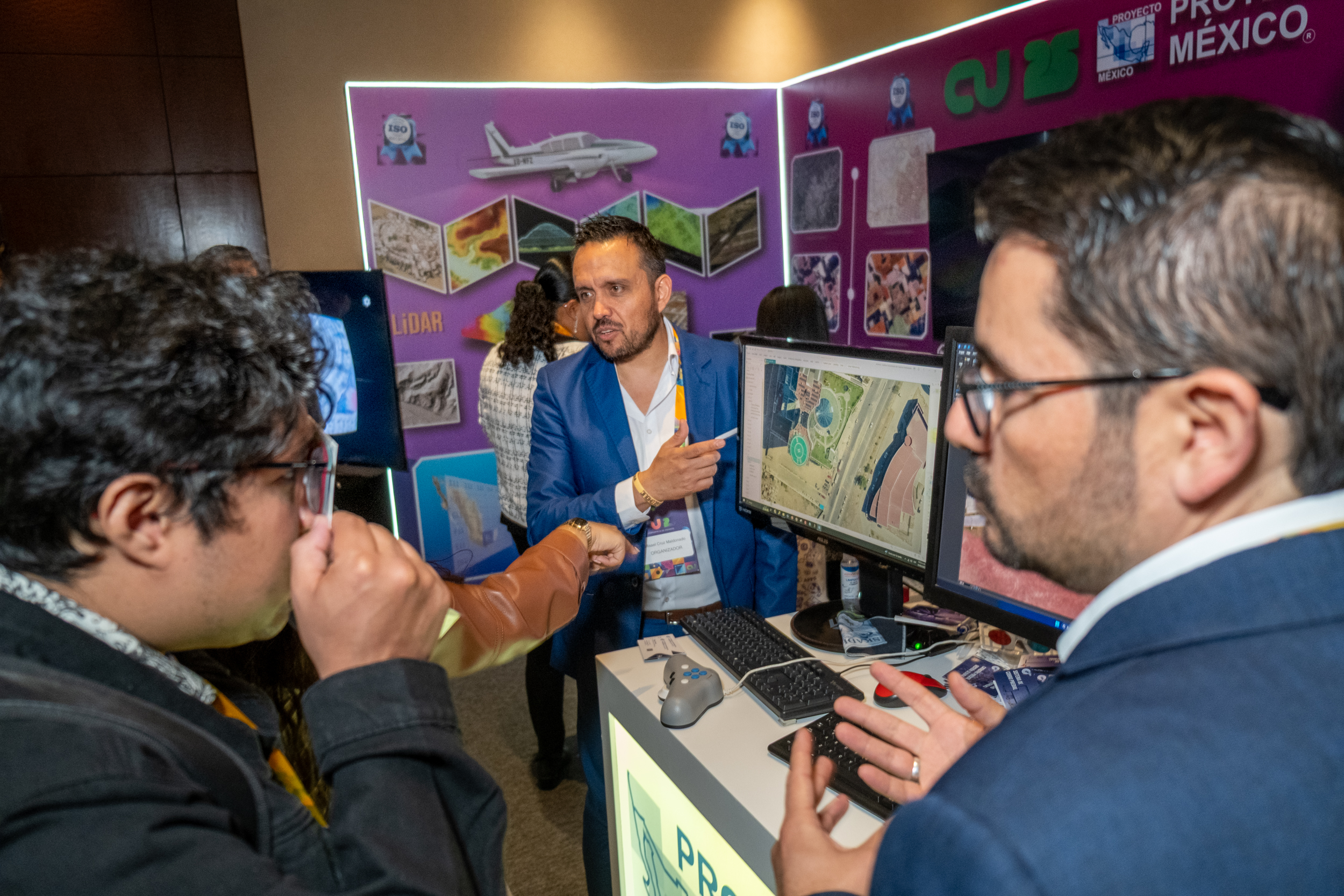 Three trade show attendees looking at a wall-mounted monitor where a map is displayed