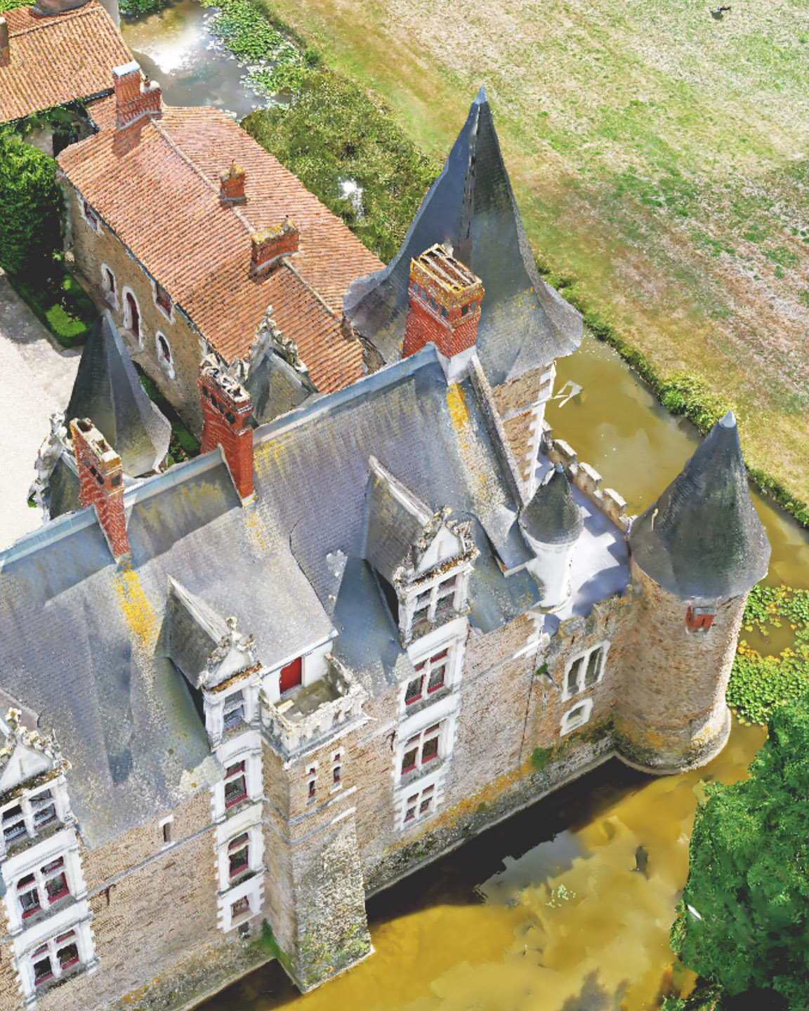 Imagen de un dron fuera del nadir de una casa de tipo castillo con un patio, rodeada por un foso y amplios campos de cultivo 