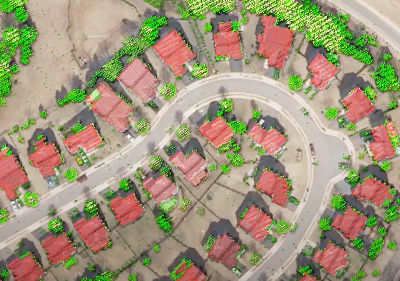 Una imagen aérea de un barrio residencial muestra estructuras resaltadas en rojo y árboles en verde.