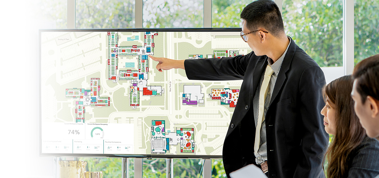 Ejecutivo mostrando a su equipo un mapa del campus con una interfaz de planificación del espacio interior y un cuadro de mandos para planificar el uso del espacio