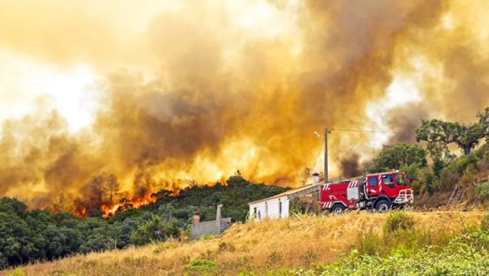 Un campo verde y herboso con colinas de vegetación en llamas anaranjadas y humo negro