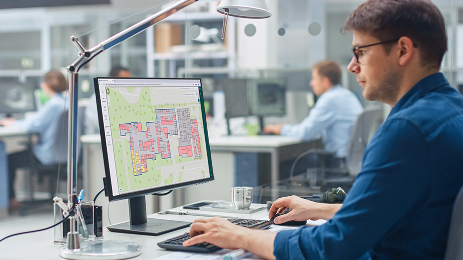 Hombre sentado detrás de un escritorio mirando un mapa de interiores con puntos de datos en un monitor de escritorio