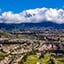 Vista aérea de suburbios con casas en estribaciones verdes, mirando hacia montañas nevadas y nubladas