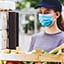 Dos personas enmascaradas interactúan sobre unas cajas de comida en un mercado agrícola
