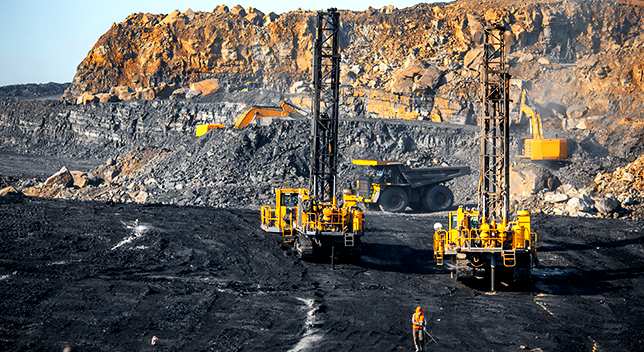 Perforadoras, excavadoras y volquetes trabajando en un campo de minas carbonizado 