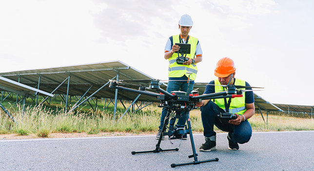 Dos trabajadores de campo con chalecos y cascos trabajando en el lanzamiento de un dron desde el suelo