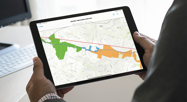 Una persona sujetando una tablet que muestra un mapa con una zona resaltada en naranja, azul y verde
