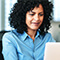 A photo of a person in a light blue collared shirt sitting at an open laptop on a desk in a sunlit modern office