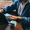 A photo of three casually-dressed people grouped around a dark wood coffeeshop table scattered with laptops and coffee cups