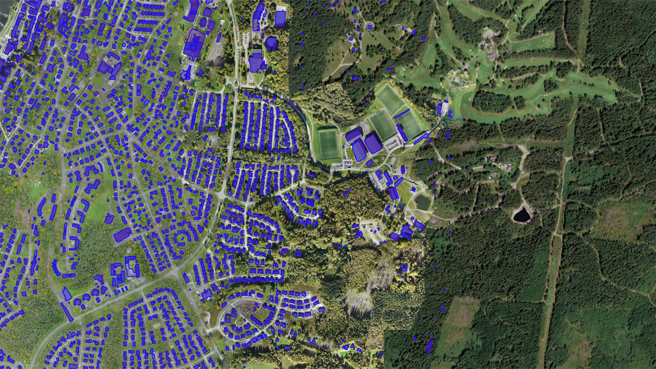 Imagen aérea de una zona suburbana con un frondoso bosque a la derecha. Los tejados están resaltados en azul, lo que indica el potencial para la instalación de paneles solares.