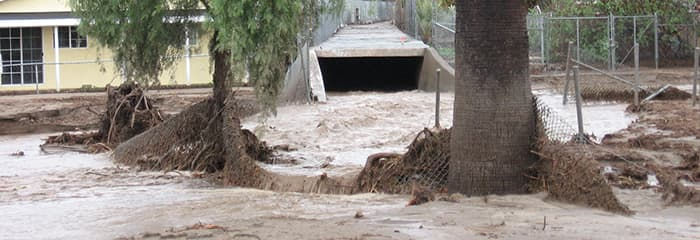 	An outlet of a flood control facility has overflowed and pours mud and water onto city streets.